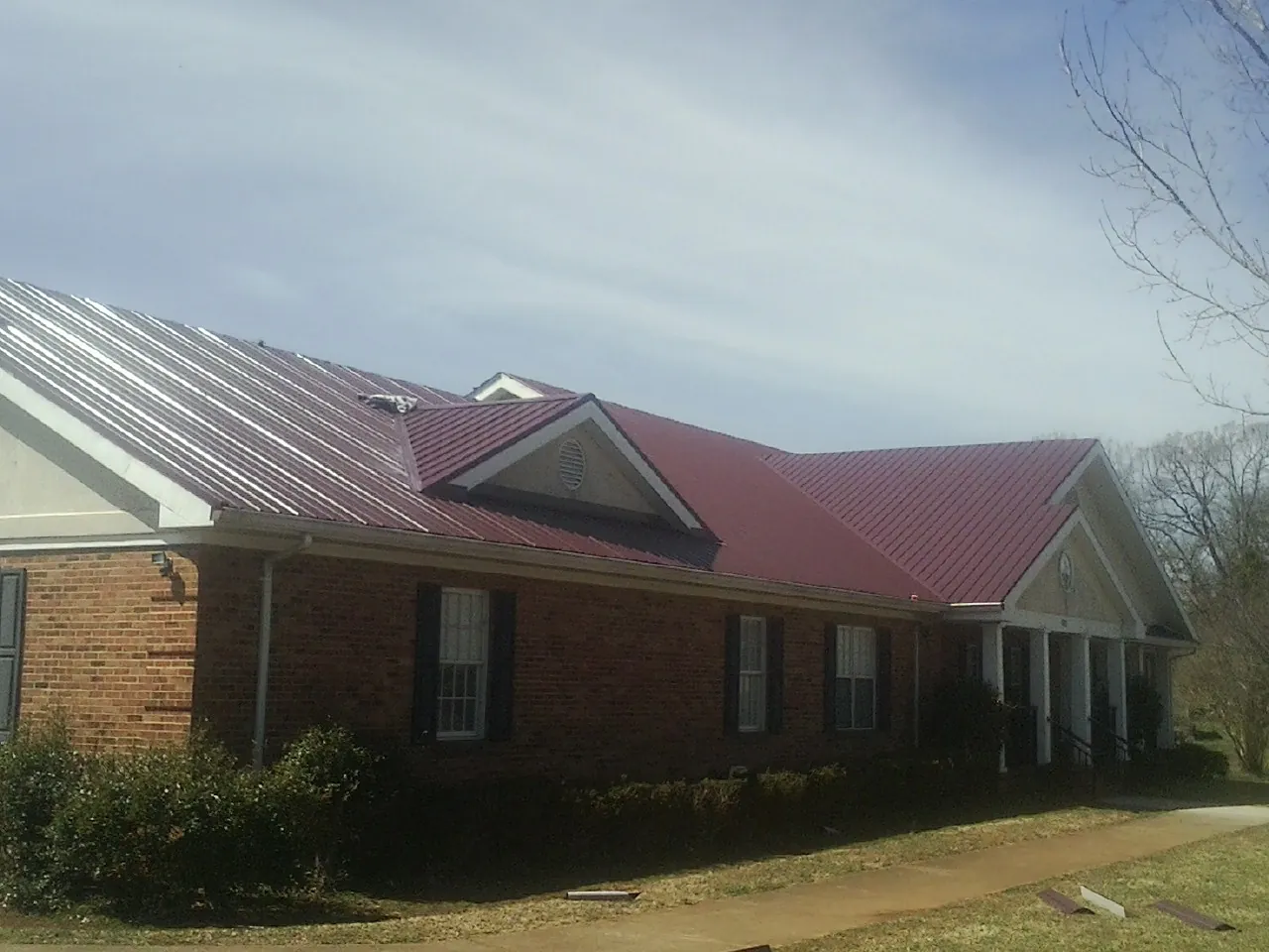 Red metal roof with gabled entries on a long brick building, from a Hail Damage Roof Repair job in White Lake