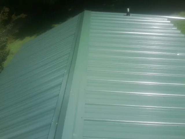 New green metal panels meeting at the ridge of a roof — Flat Roof Repair work by our crew in White Lake
