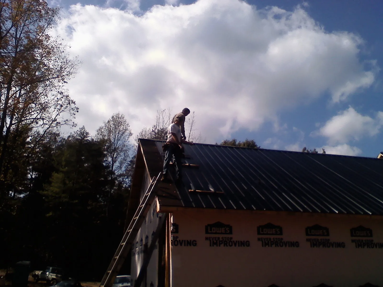 Roofer fastening dark metal panels high against a cloudy sky, from a Roof Inspection job in White Lake