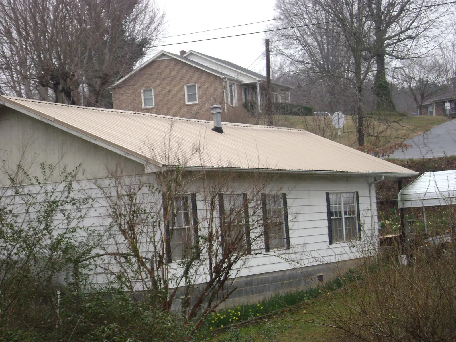 Tan metal roof on a white sided house set into a hillside — Commercial Roofing by Roofing Brothers in White Lake