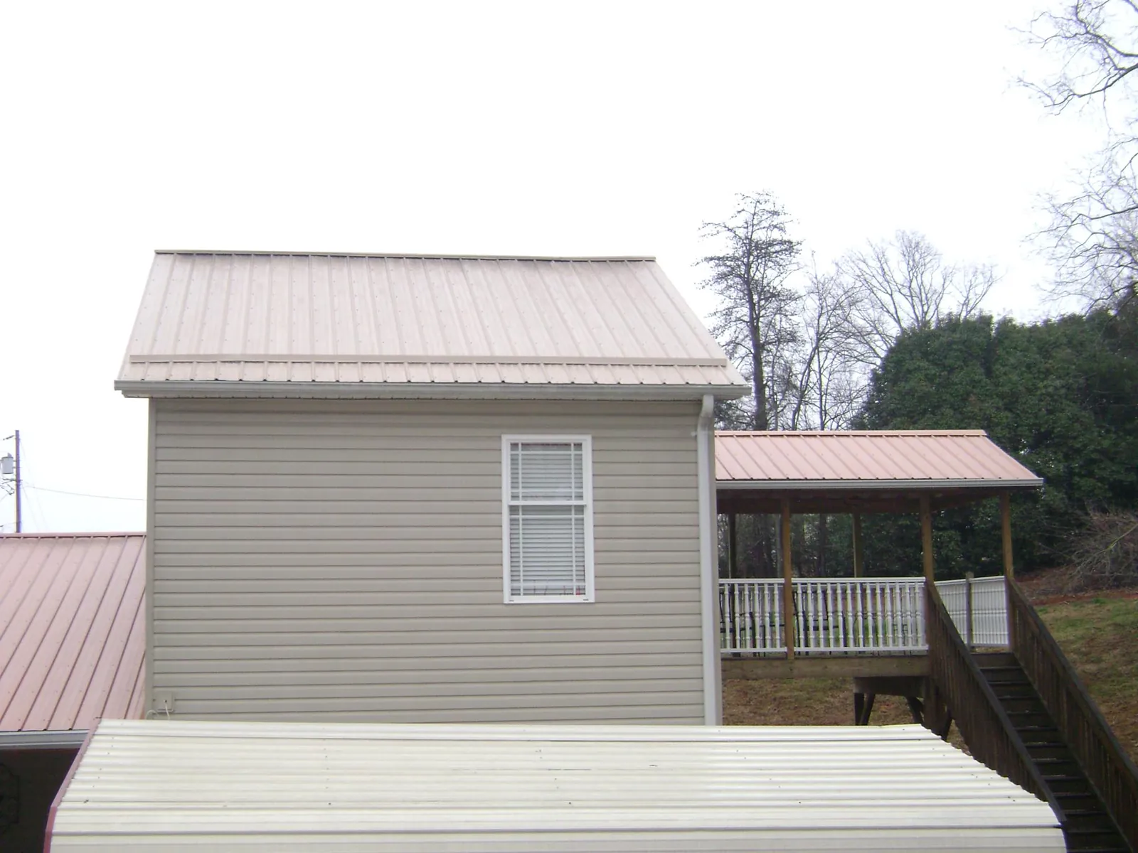 Tan metal roofs on a two story addition and attached porch, from a Roof Replacement job in White Lake